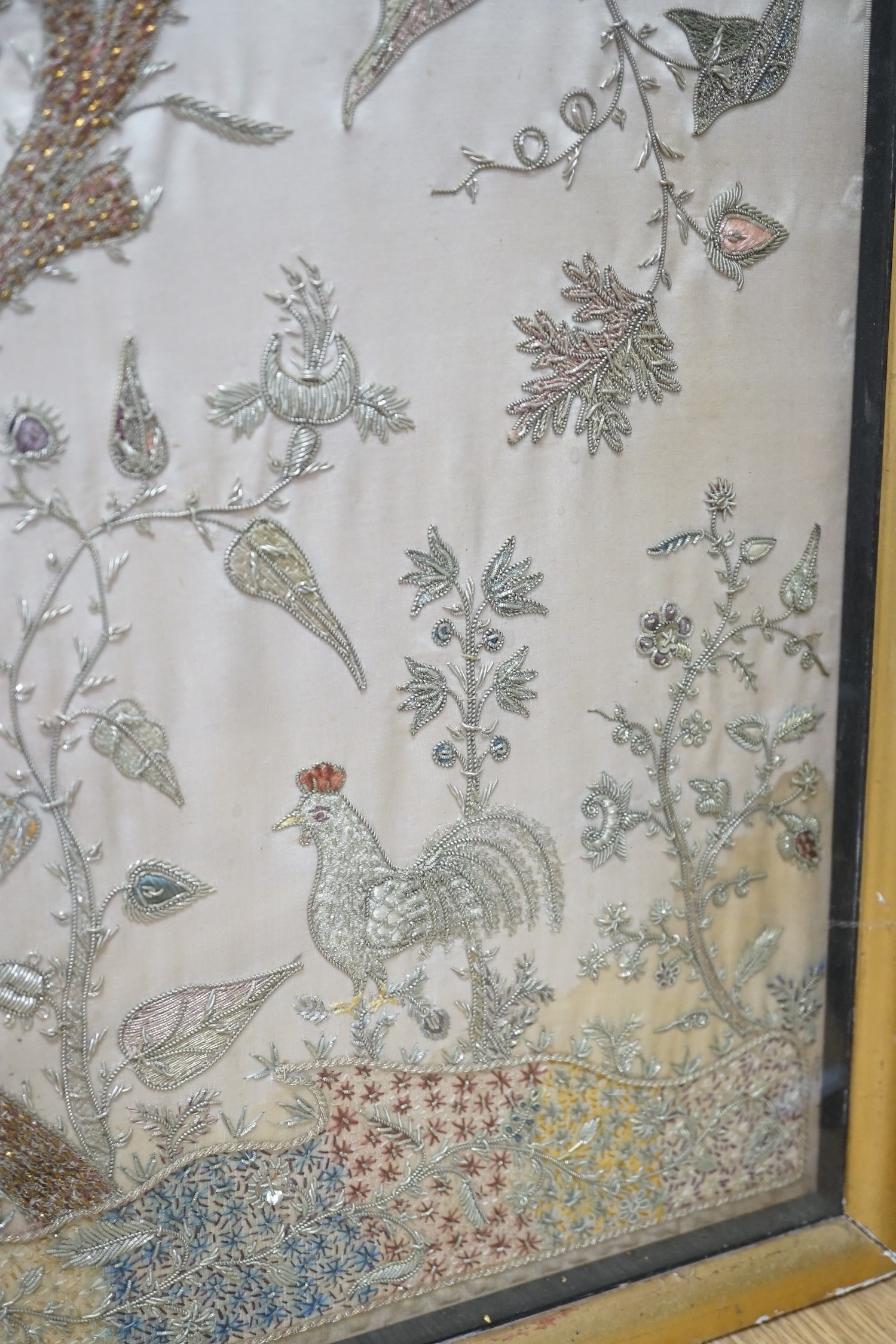 A framed silk, multi coloured metal thread embroidered Indian panel: a peacock seated amongst birds, flowers and leaves in a tree, 110cms x 51cms